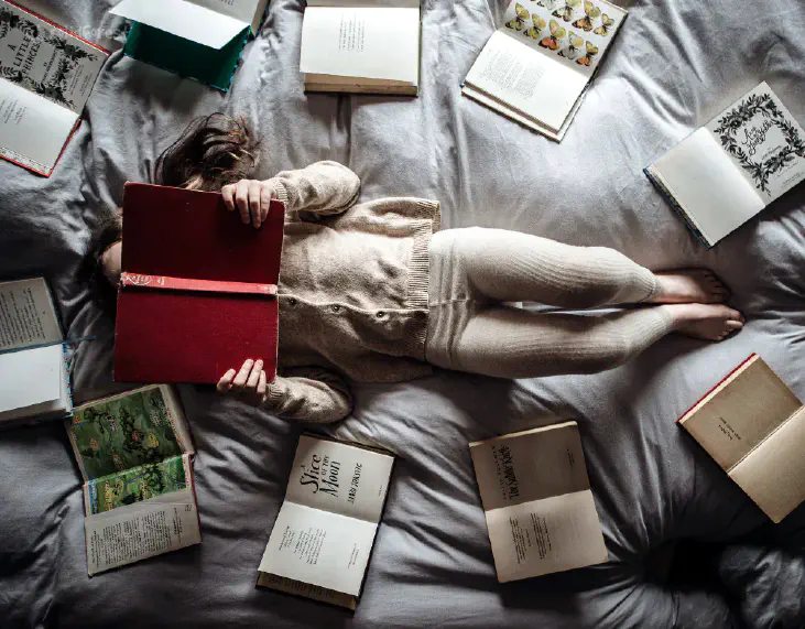 A girl reads a book while lying in bed