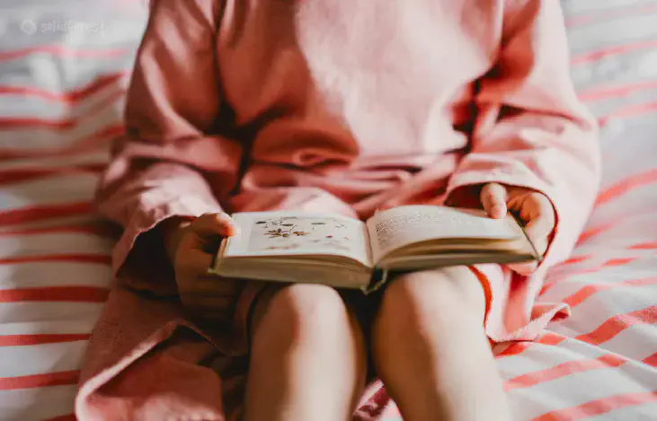 A girl reads a book placed on her thigh