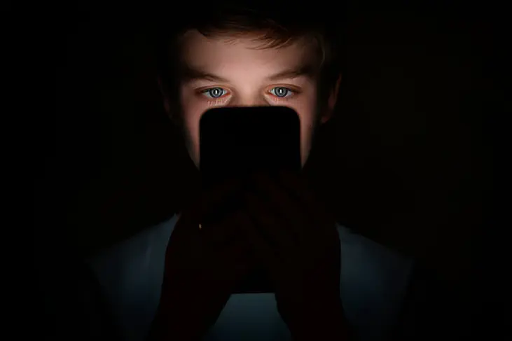 A boy in the dark looking to his phone screen