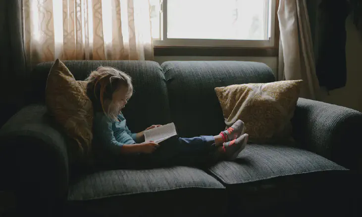 girl reading book sitting on sofa.