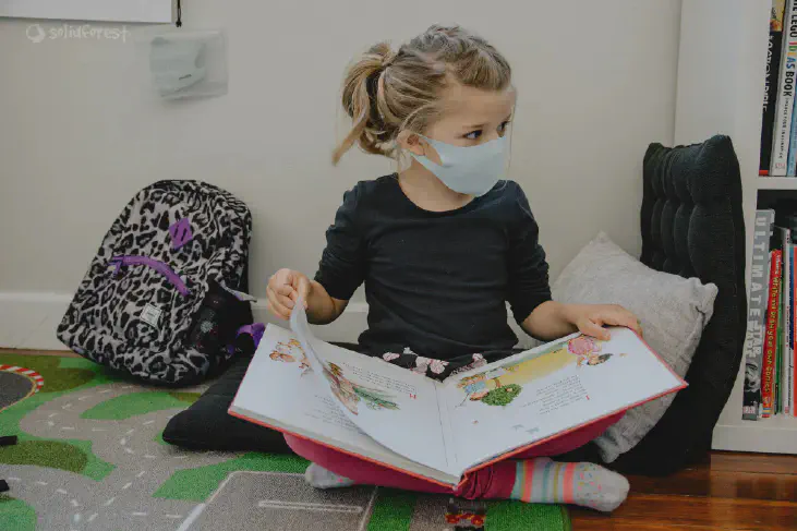 A girl using face masker reading book sitting on mat