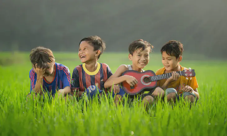 Four boys laughing and sitting on grass during daytime